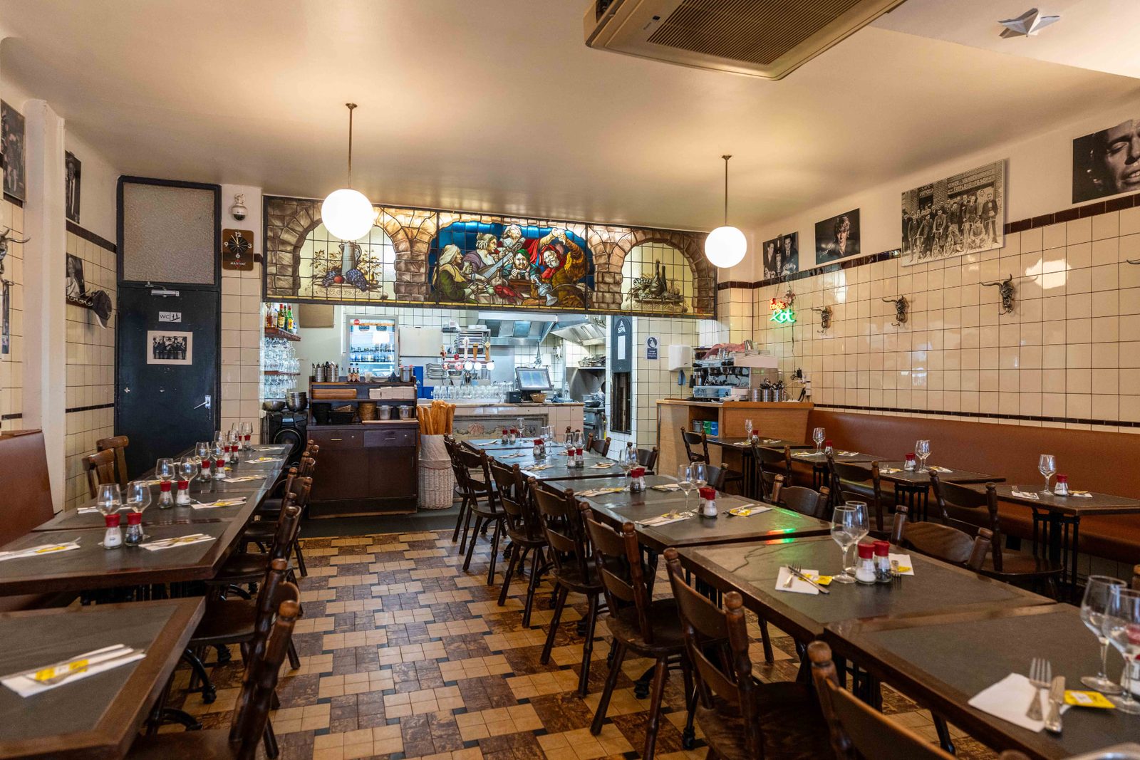 Salle du Pré Salé rue de Flandre : carrelage blanc d'origine, tables en bois dressées et vitrail brueghelien au-dessus de la cuisine ouverte